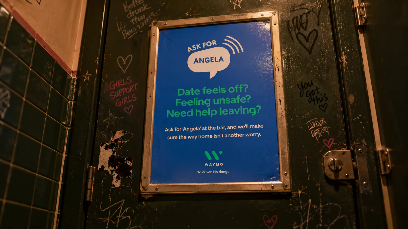 Waymo Ask for Angela poster on a graffitied nightclub toilet door