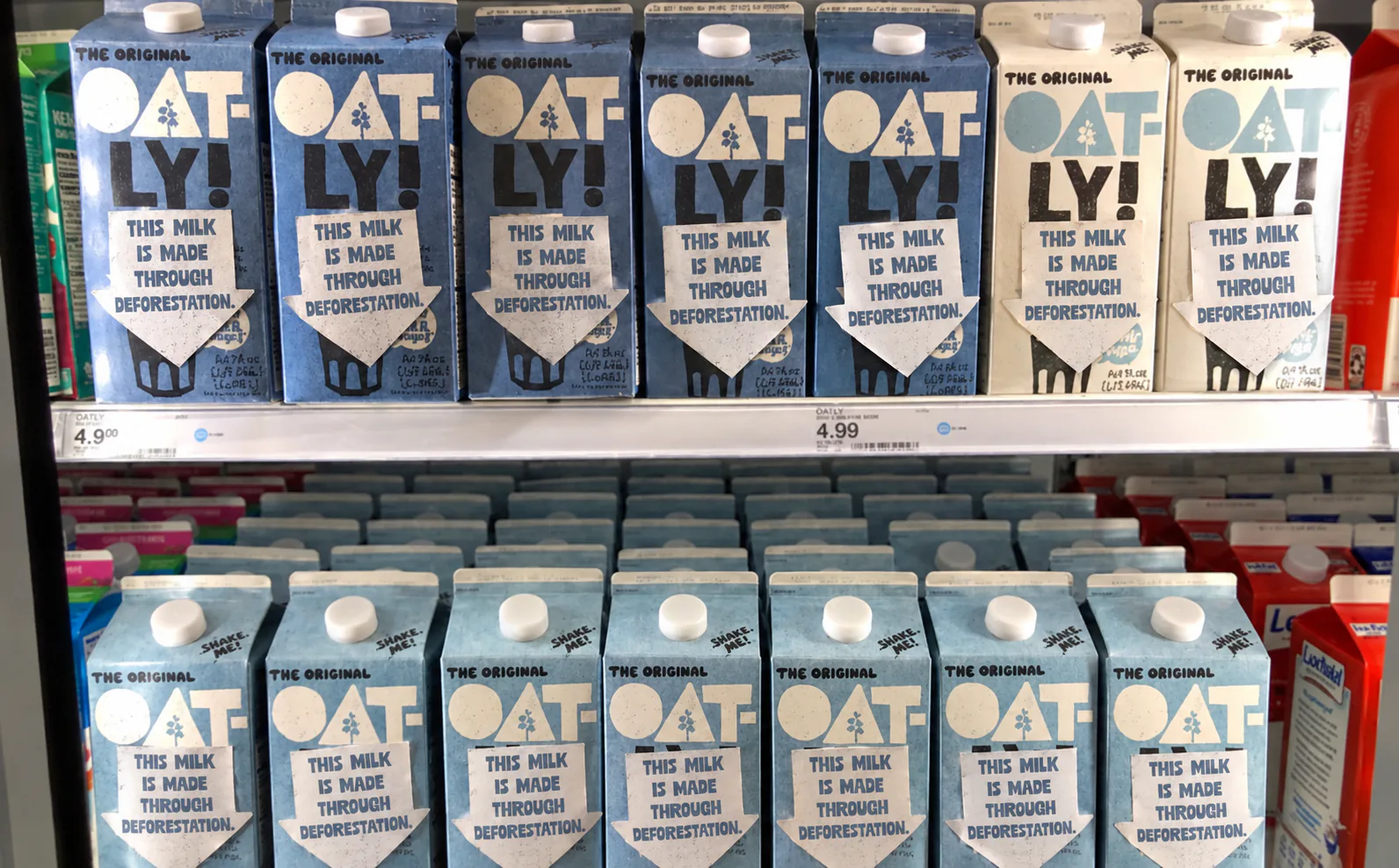Oatly cartons on a shelf with stickers: this milk is made through deforestation